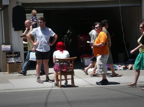 Red haired woman sitting in chair on sidewalk with people walking past
