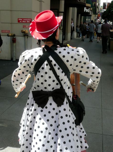 woman in red cowboy hat with polka dotted dress walking with bass drum